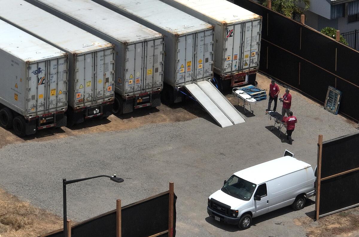 Workers stand next to refrigerated storage containers for bodies.