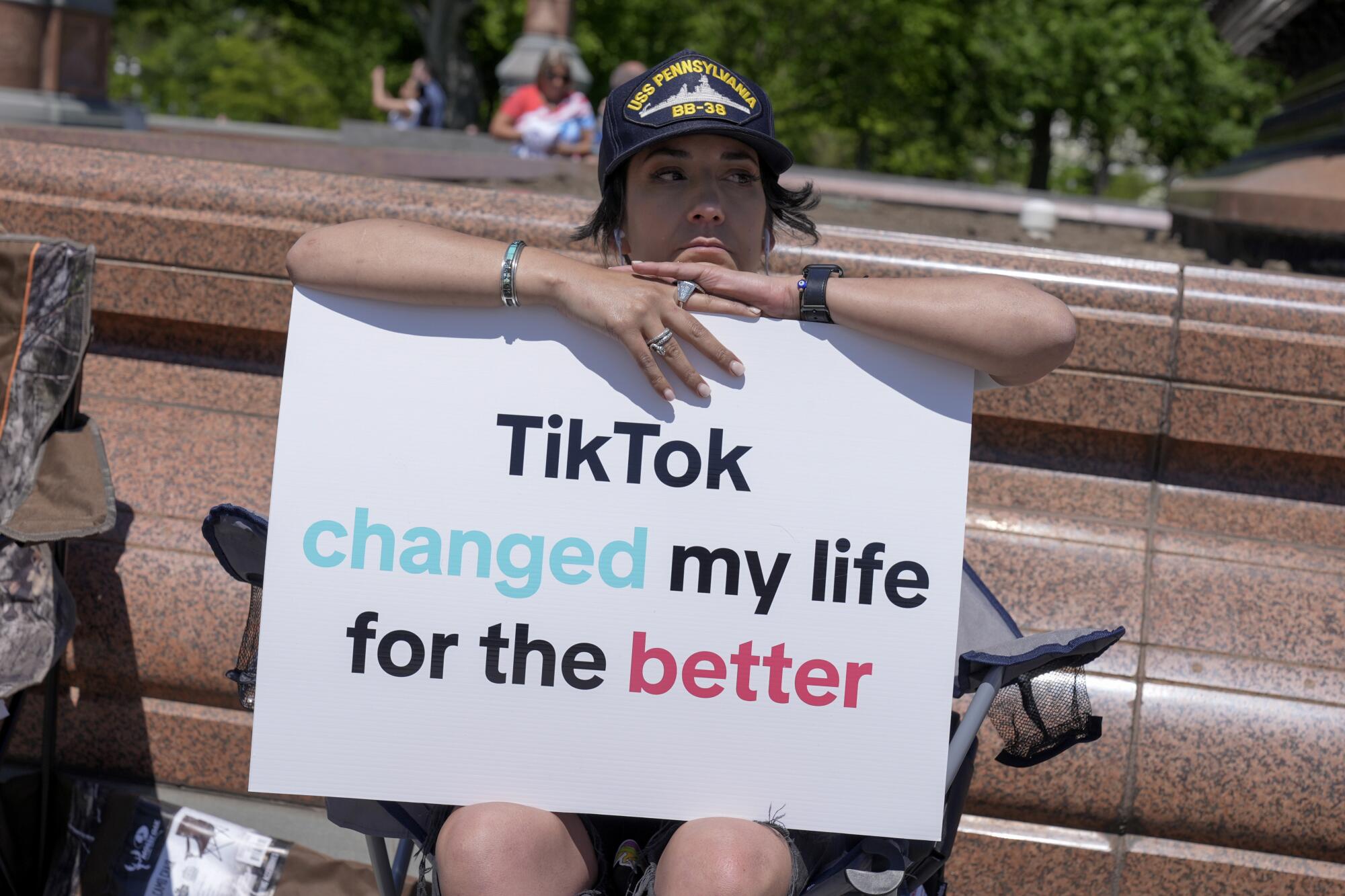 A person sitting in a folding chair with a sign reading, "TikTok changed my life for the better"