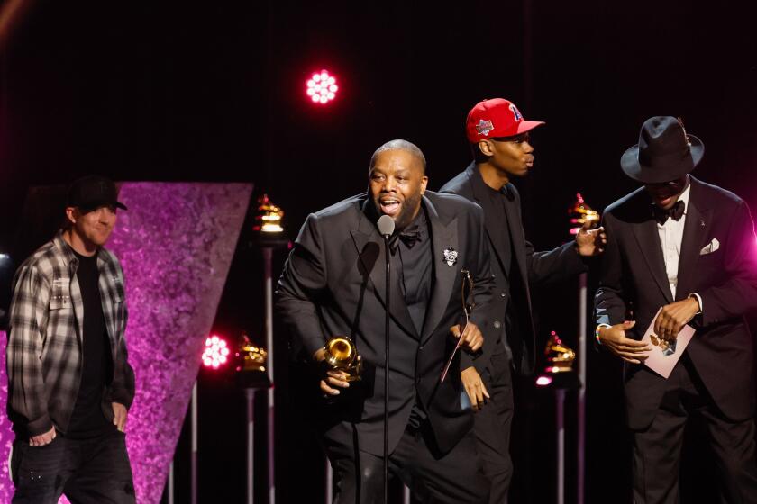 Killer Mike in a black suit holding a Grammy Award in his right hand speaking in a microphone at the Grammys.