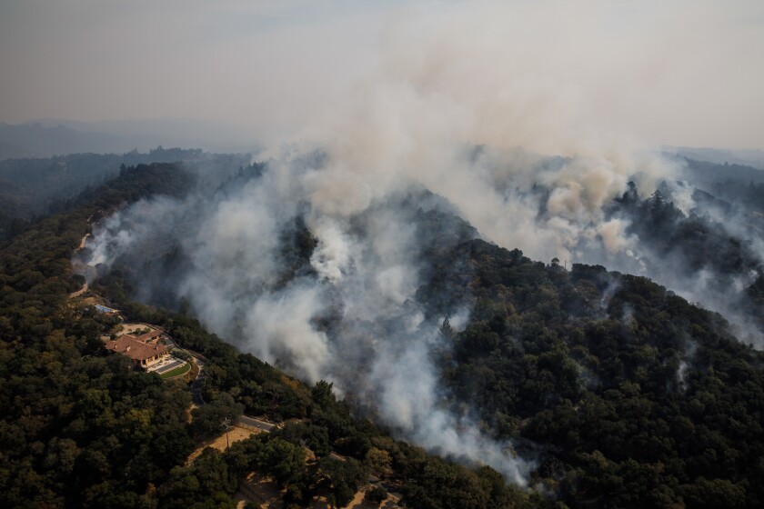 A home perched on top of a hill sits in the foreground of a fire moving up on Shiloh Ridge near Santa Rosa.