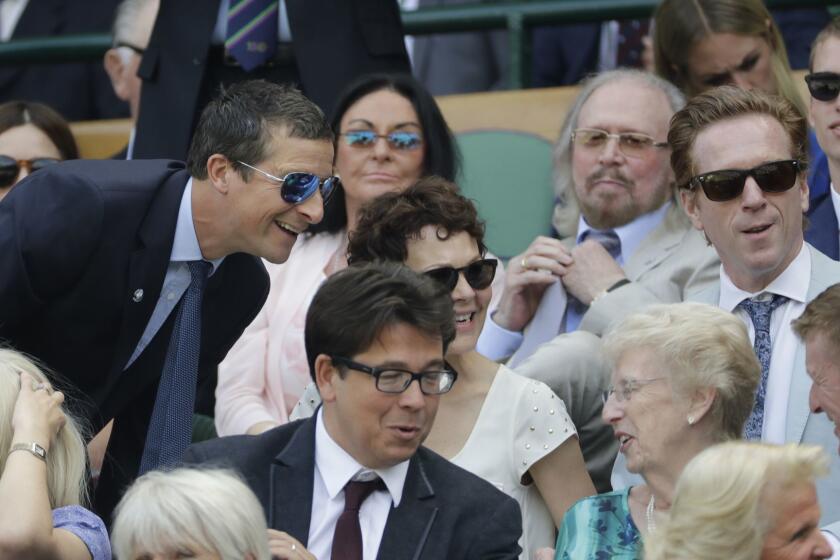 Actors Damian Lewis, right, and Helen McCrory, center, and Bear Grylls, left, sit in the Royal Box on Centre Court ahead of the men's singles semifinal match between John Isner of the United States and South Africa's Kevin Anderson at the Wimbledon Tennis Championships, in London, Friday July 13, 2018. (AP Photo/Ben Curtis, Pool)