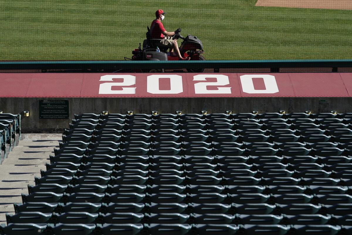 A member of the grounds crew rides a mower past empty stands before Los Angeles Angels baseball practice.