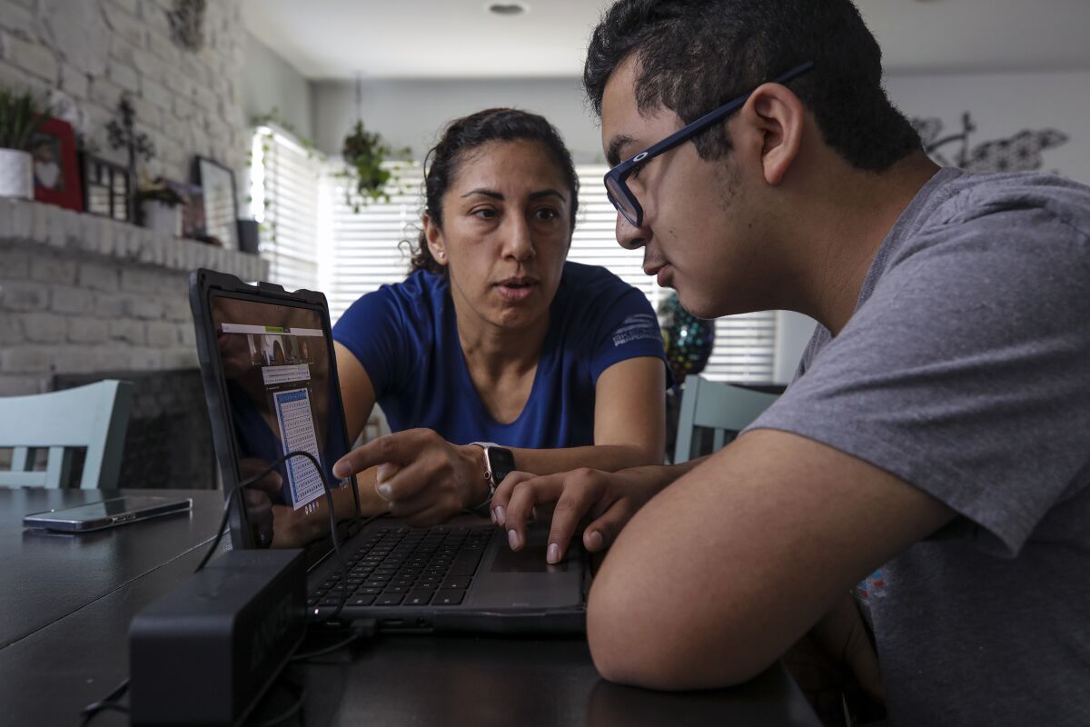 Sandra Torres helped her 14-year-old son Diego Torres, during a class on zoom at home in June. 