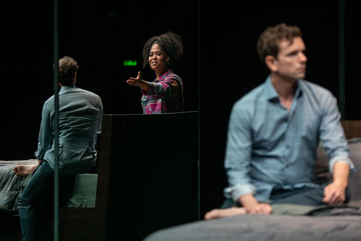 A woman gestures to a man sitting on a bed as they're reflected in a mirror in "Slave Play" at the Mark Taper Forum.