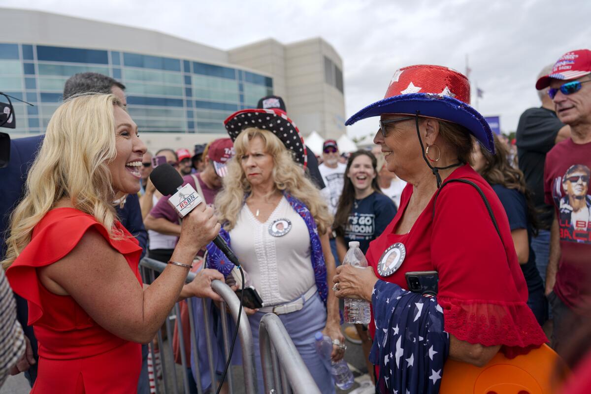 Marjorie Taylor Greene holds a microphone and faces a crowd wearing red, white and blue