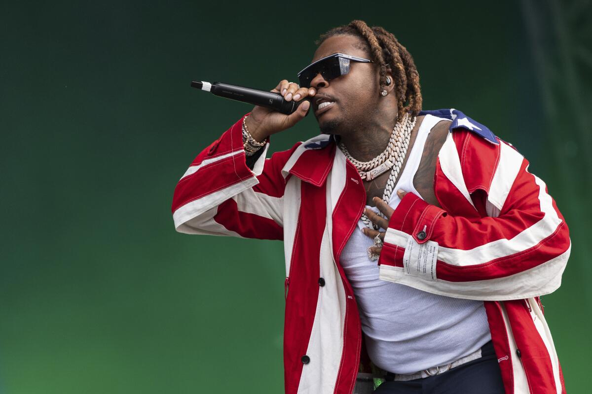 Gunna, wearing a red-and-white-striped jacket, a white shirt, chains and sunglasses, holds a microphone to his mouth onstage