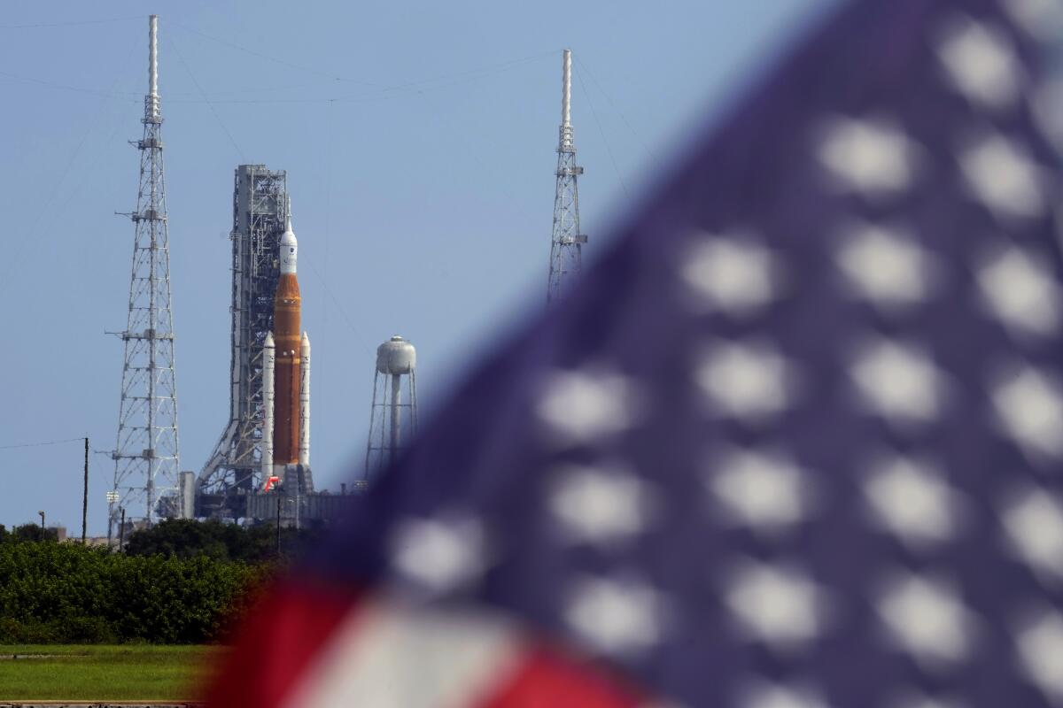 An American flag flies in the breeze as NASA's new moon rocket sits on a launch pad.