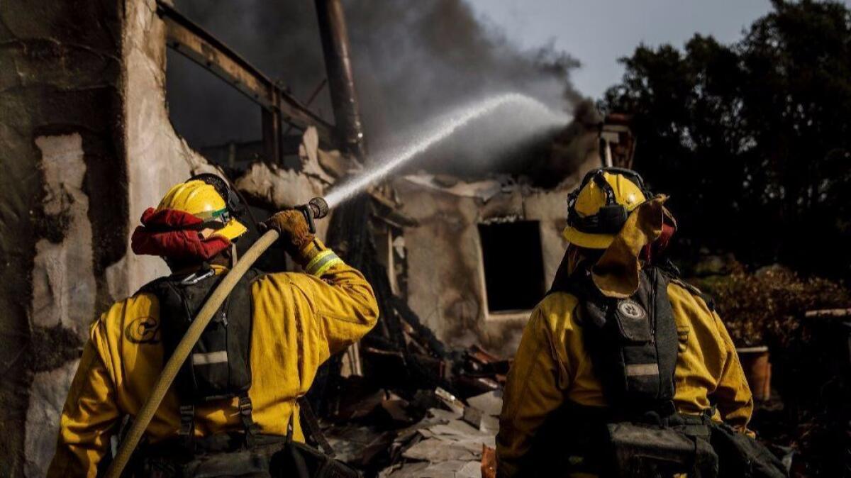 Humboldt County firefighters Bobby Gray, left, hoses down smoldering flames inside a destroyed home, as Kellee Stoehr, right looks on, after the Thomas Fire burned in Montecito.