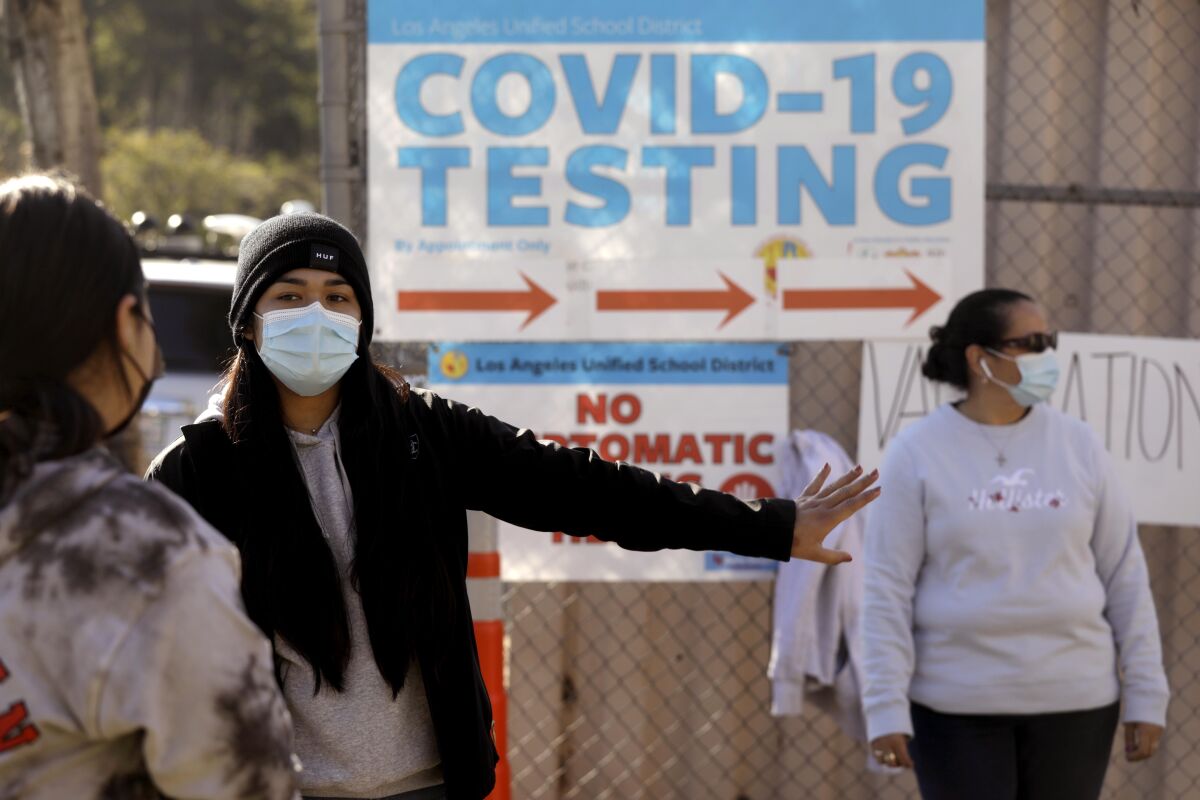 People stand around a sign reading "COVID-19 Testing."