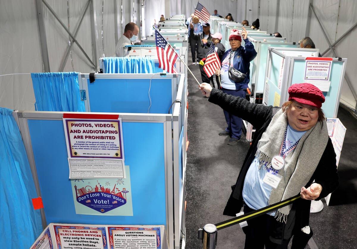 Election workers using small American flags to point voters to open voting booths at a busy polling place.