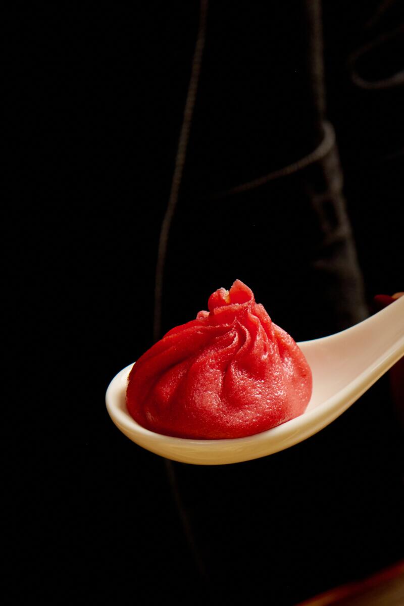 A spoon holds one red soup dumpling.