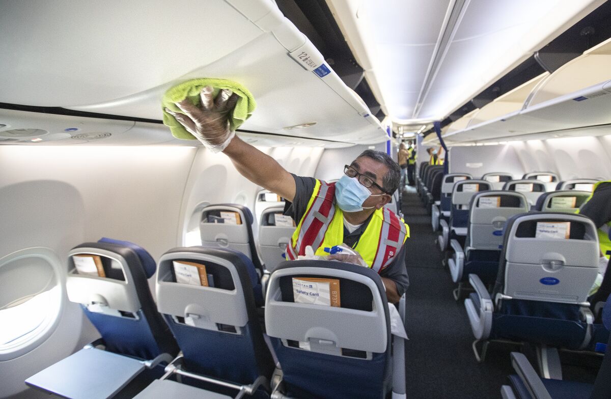 A worker wearing a face mask leans on a seat inside a plane as he cleans with a cloth.