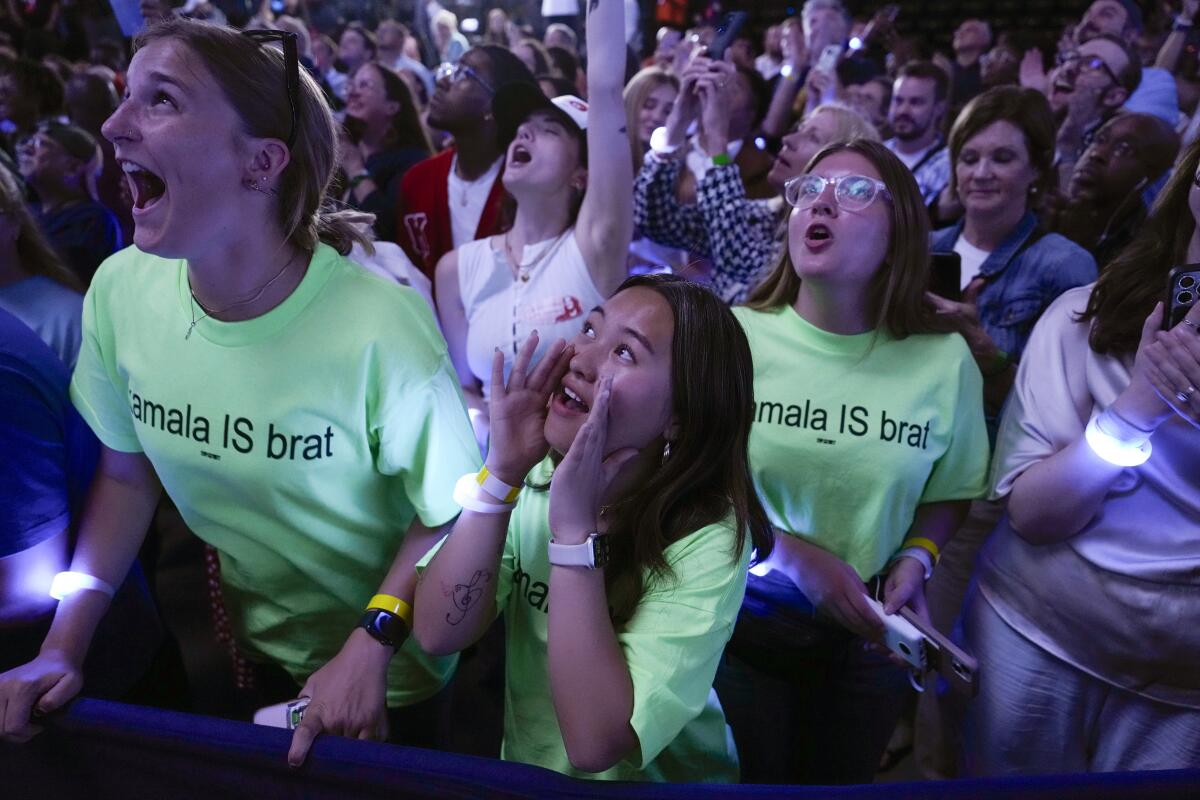 Crowd members wear "Kamala IS brat" T-shirts and cheer.