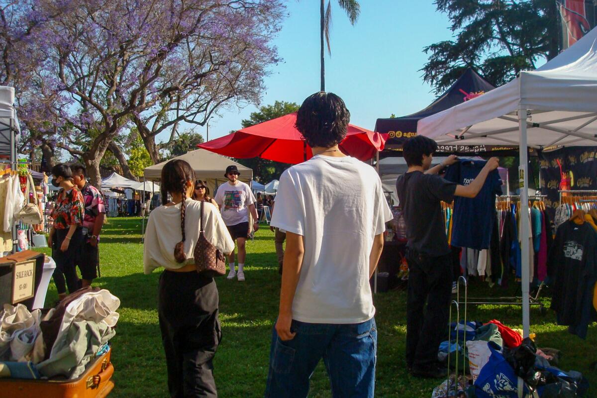 People walk past stalls under umbrellas and pop-up tents outdoors.