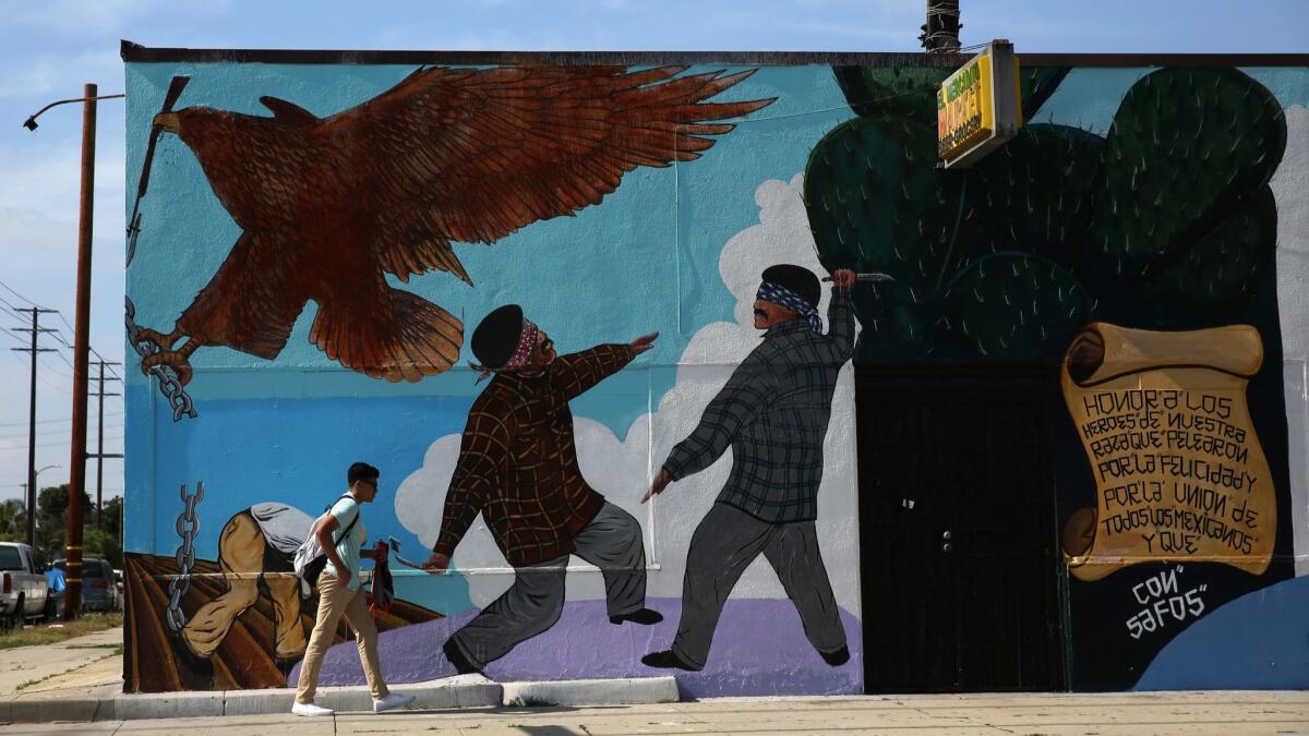 A person walks past the landmark mural on "El Mercadito Market," which depicts rival Eastside and Westside Wilmas gang members.