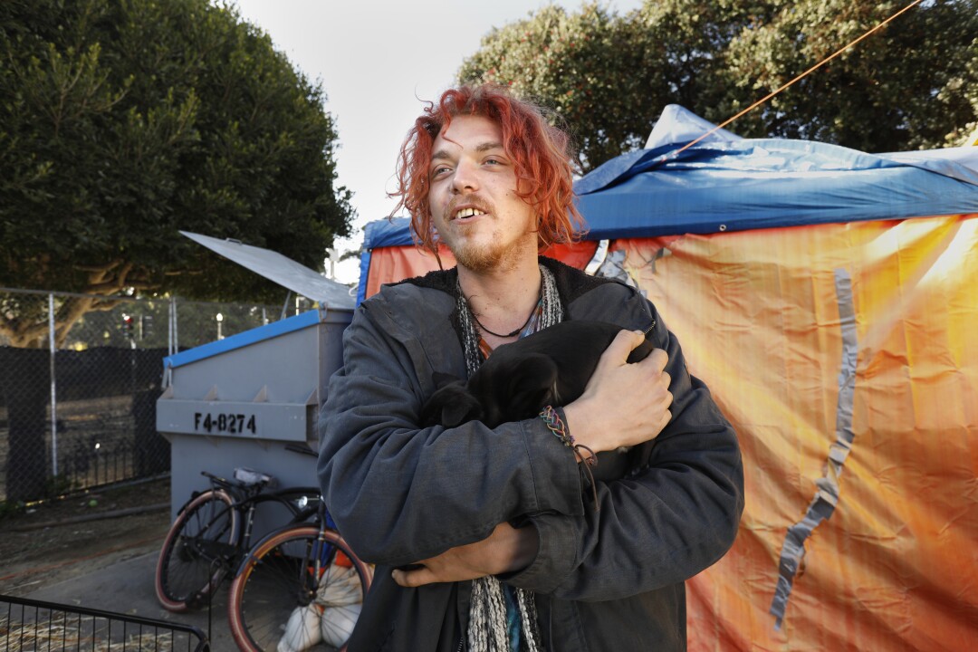 A man holds a black puppy outside a tent