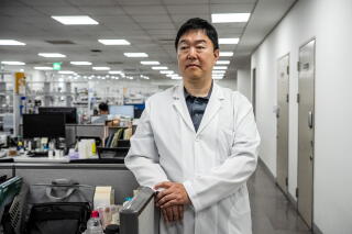 a man in a white lab coat stands for a portrait