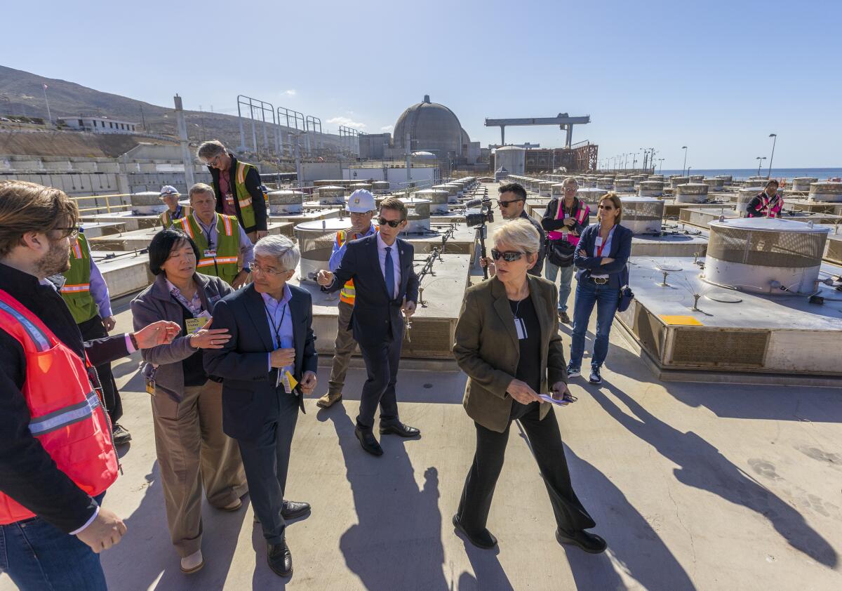 A small group of people, some of them wearing reflective vests, stand outdoors at a power plant.