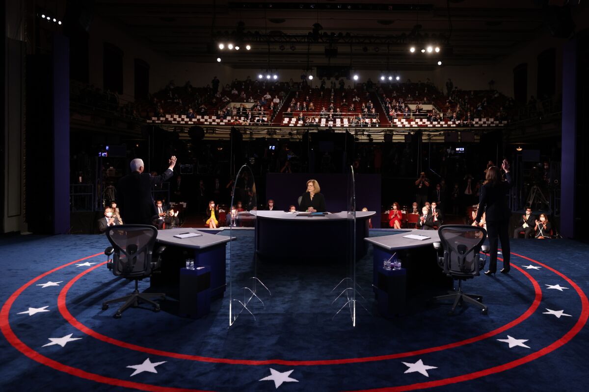 Kamala Harris and Joe Biden stand on red white and blue carpeted stage, waving to sparse crowd in debate hall