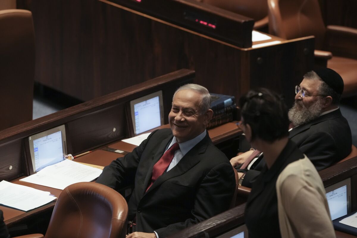 Benjamin Netanyahu smiles while sitting in a seat at the Knesset
