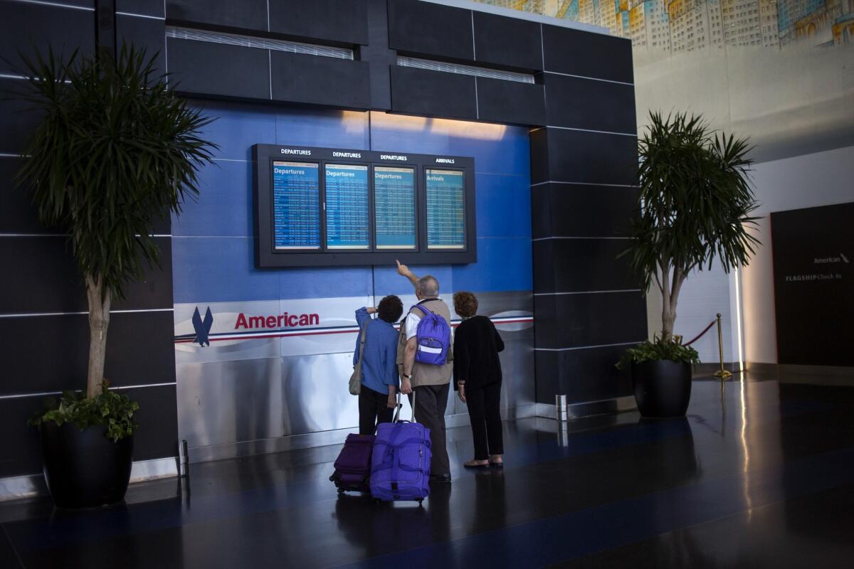 Travelers check flight times in the American Airlines/US Airways Terminal at John F. Kennedy Airport in New York. American Airlines now charges $150 to escort an unaccompanied minor ages 12 to 14.