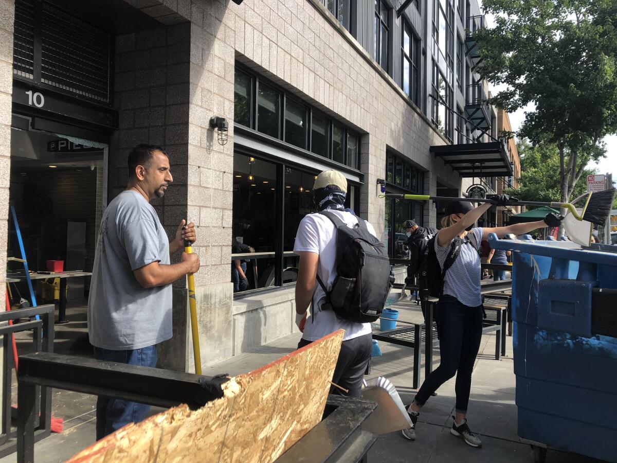 Manny Hundal cleans up glass from the broken windows of his pizza shop after vandals broke them during protests on Sunday.