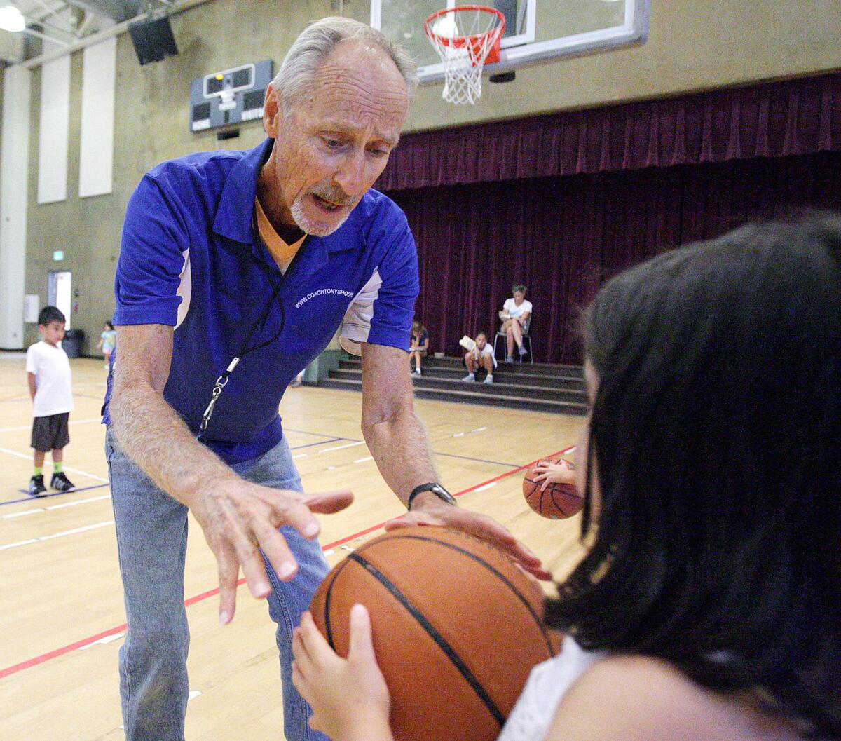Camp director Tony Passarella goes from player to player, including Kelin Shajanian, 6, of Glendale, to go over how to properly hold a basketball and make a chest pass at the annual Basketball, Training and Fitness Camp at Pacific Park Community Center in Glendale on Thursday, July 23, 2015.
