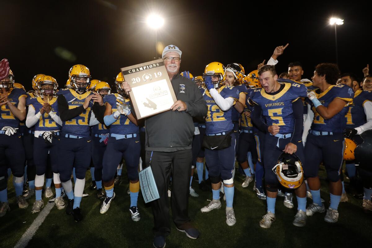 Marina coach Jeff Turley, center, holds up the championship plaque as the Vikings celebrate after beating Muir 18-9 in the CIF Southern Section Division 11 title game at Westminster High on Nov. 29, 2019.