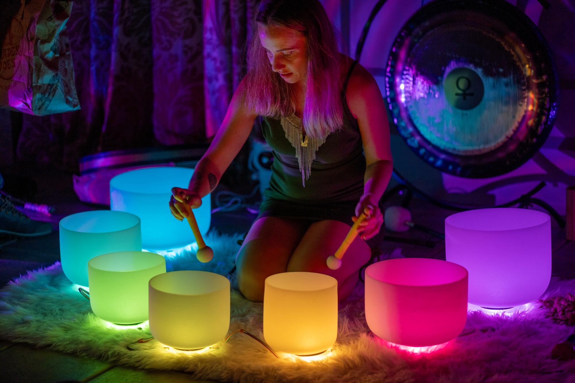 A woman plays crystal singing bowls alight with an array of colors.