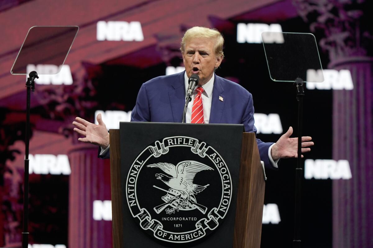 Former President Trump speaks at a dais with a National Rifle Assn. logo with "NRA" repeated in the background. 