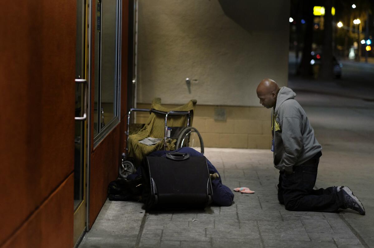 Anthony Ruffin, 48, kneels to speak with a homeless man as he is sleeping on the sidewalk in Hollywood.