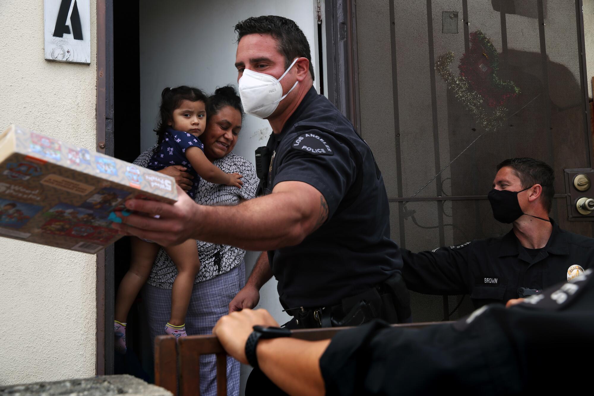 Los Angeles Police Officer Nick Ferara, center, with Officer Dan Brown, right, gives Victoria Taboada a game for her 3-year-old daughter in San Pedro