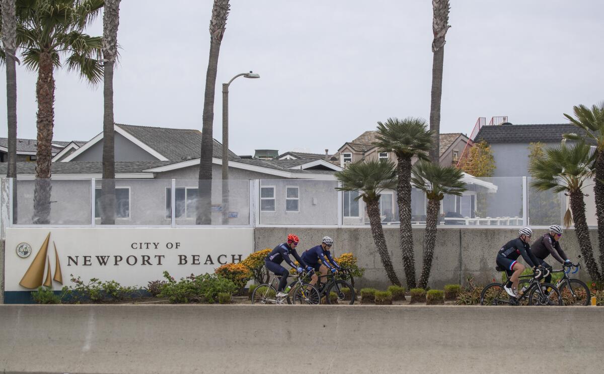 People ride bikes past a sign welcoming them to Newport Beach on March 31.