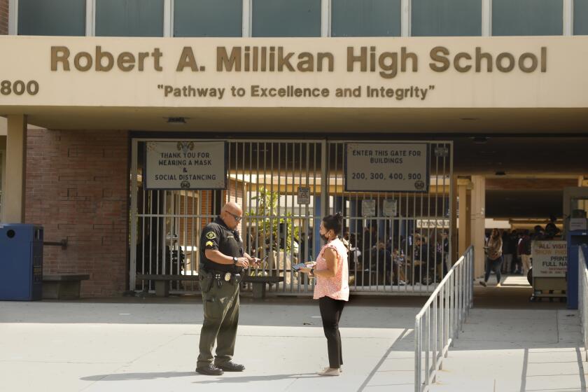 Long Beach, California-Sept 29, 2021-A Long Beach Unified School District officer speaks to a woman outside Robert A. Millikan High School in Long Beach on Sept. 29, 2021. (Carolyn Cole / Los Angeles Times)