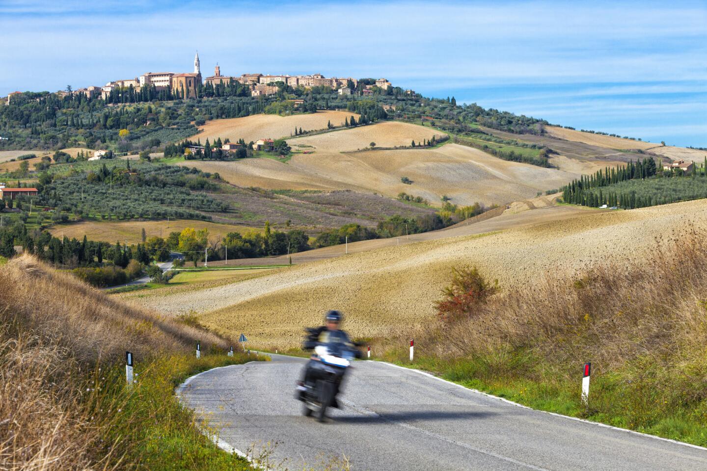 A motorcyclist navigates a winding road out of Pienza in Tuscany, Italy.