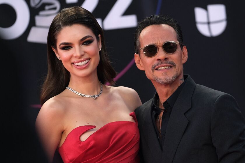 woman with long brown hair worn down in red strapless dress smiles next to man with short hair, black sunglasses and suit