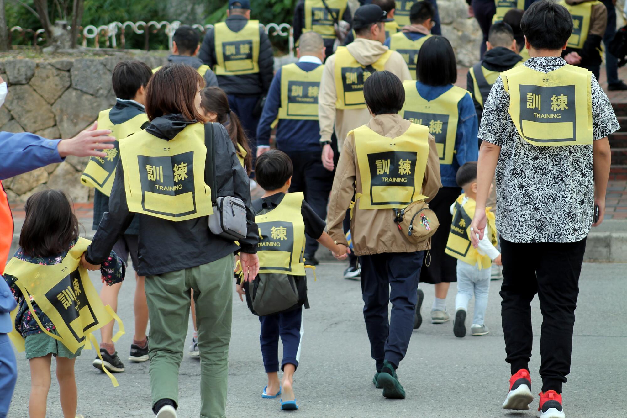 People wearing yellow bibs walk to a field for a missile drill on Japan's Ishigaki island.