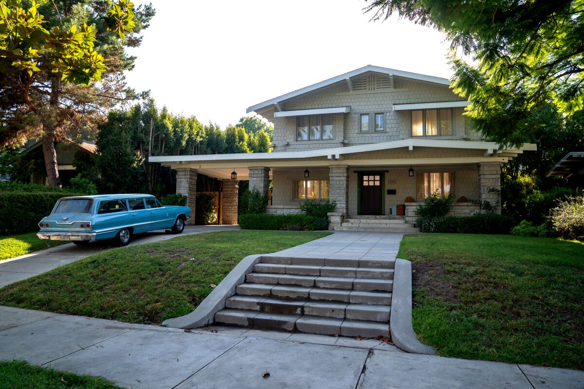 A two-story Craftsman home has a station wagon from the 1960s in the driveway for
