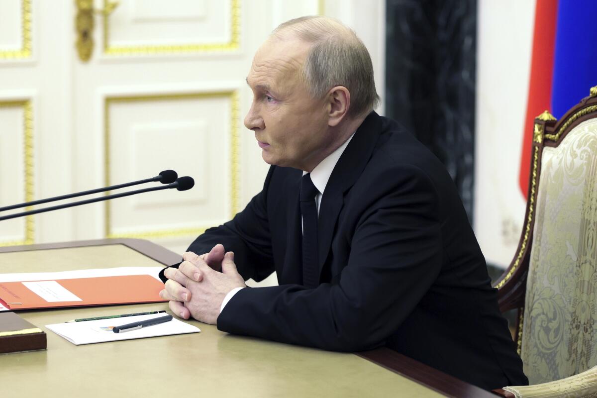 Russian President Vladimir Putin sits at a table.