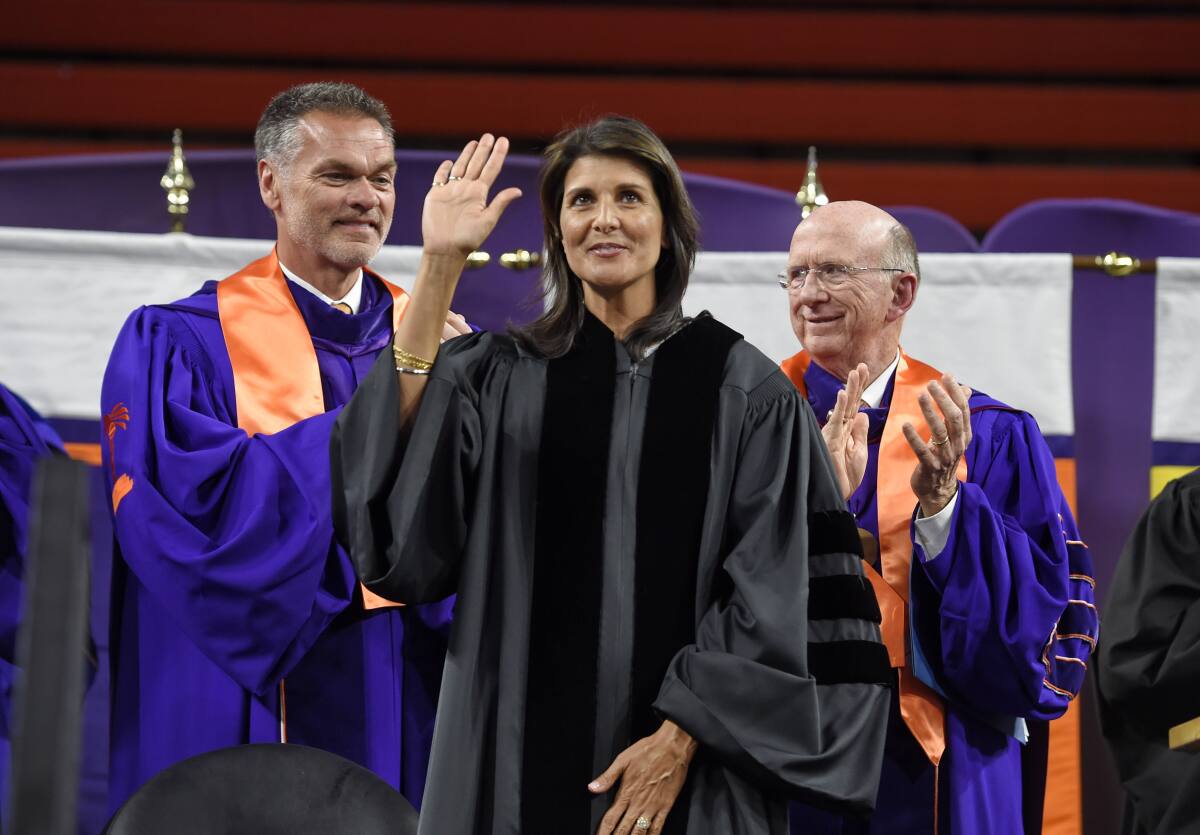 FILE - In this May 10, 2018 file photo, Clemson board of trustees members, William C. Smith, left, and David H. Wilkins applaud while UN Ambassador Nikki Haley, a 1994 Clemson graduate, waves to the crowd before she gives the 2018 Commencement speech in Clemson, S.C. As she ponders her next political steps, Haley has accepted a lifetime appointment to the the Board of Trustees of Clemson University, her alma mater. The university made the announcement on Tuesday, Oct. 12, 2021. (AP Photo/Richard Shiro, File)