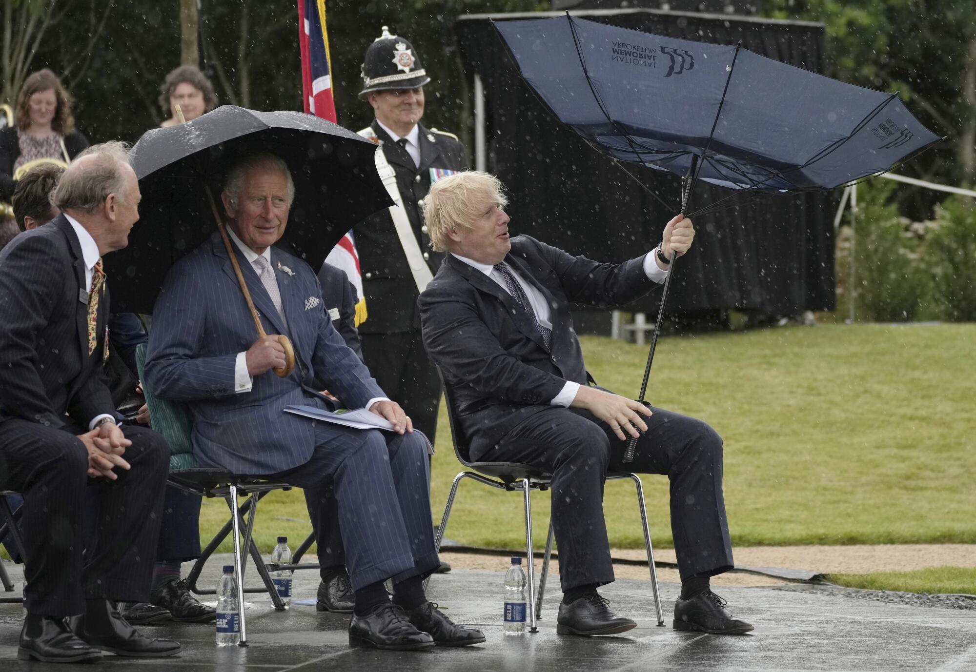 Britain's Prince Charles, center, and Prime Minister Boris Johnson, right, shelter from rain 