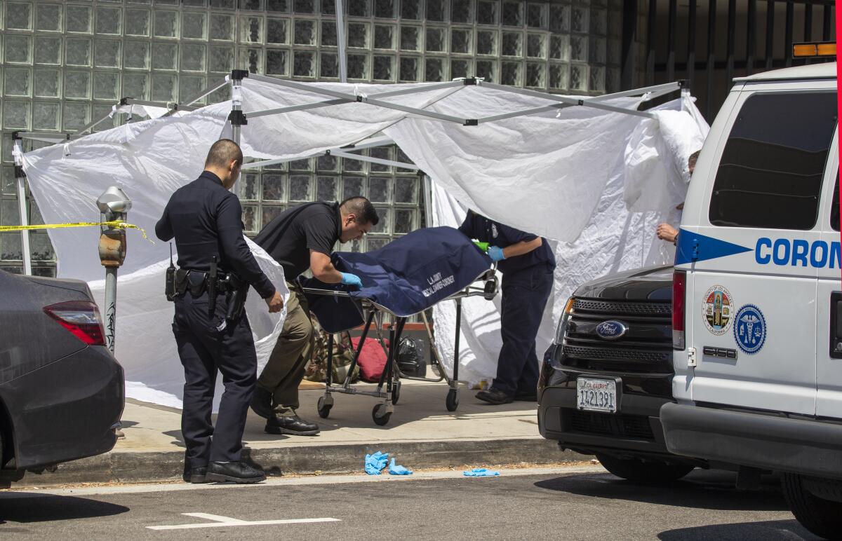 Un oficial de LAPD inspecciona mientras el investigador Adrián Muñoz, al centro, de la oficina forense del condado de Los Ángeles, retira el cuerpo de Alvin Robinson cerca de la intersección de la avenida Massachusetts y el bulevar Sepúlveda.