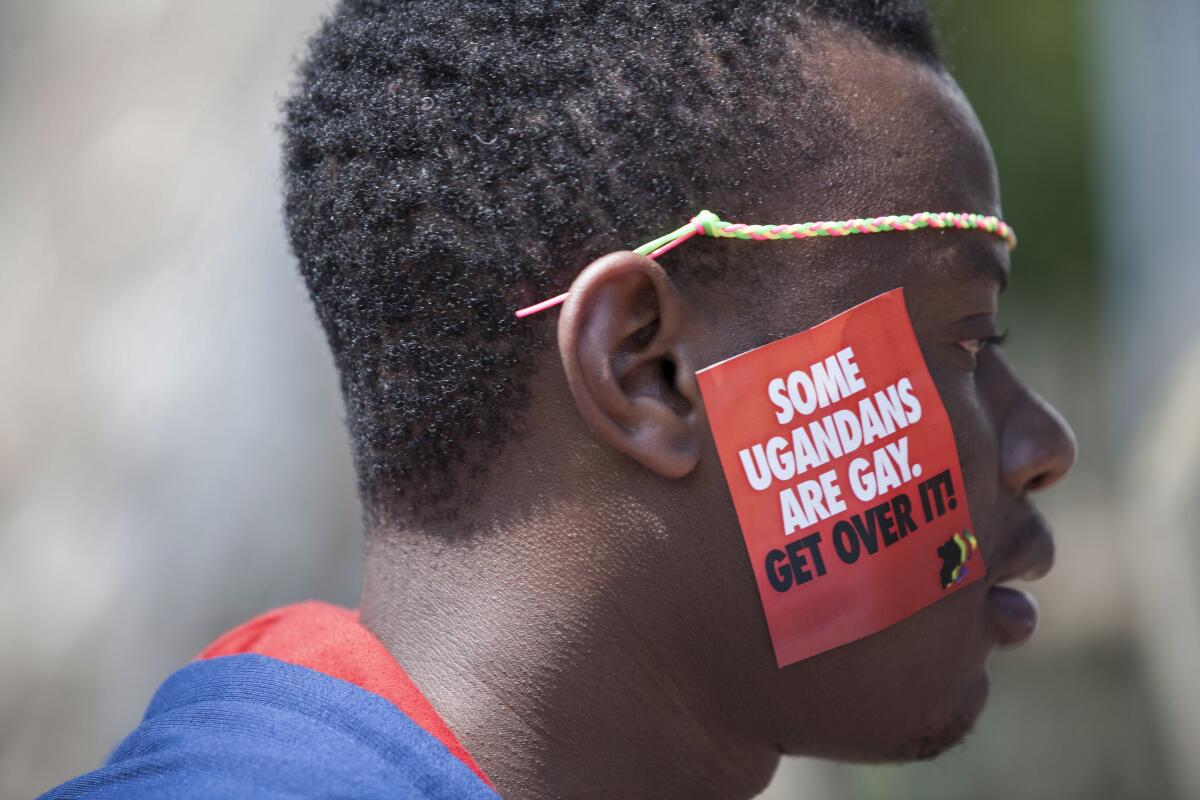 A closeup of a man wearing a red sticker on one cheek that says, "Some Ugandans are gay. Get over it!"