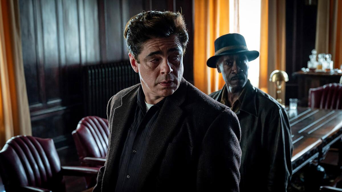 Benicio del Toro, left, and Don Cheadle stand in a well-appointed room.