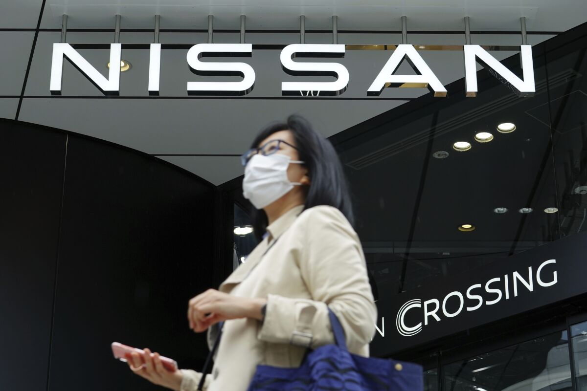 A woman wearing a face mask to to help curb the spread of the coronavirus walks by the logo of Nissan seen at the automaker's showroom in Tokyo Tuesday, May 11, 2021. Nissan reduced its losses for January-March, compared to last year, as restructuring efforts kicked in, despite the sales damage from the coronavirus pandemic, the Japanese automaker said Tuesday. (AP Photo/Eugene Hoshiko)