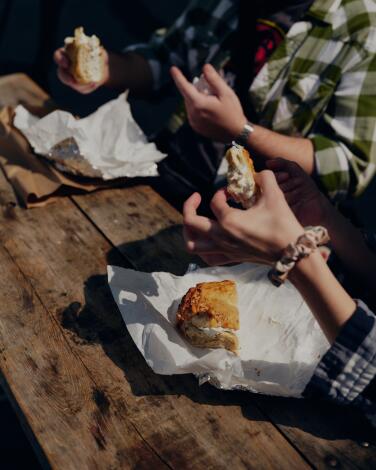 Hands holding bagels above paper wrapping on a wood table
