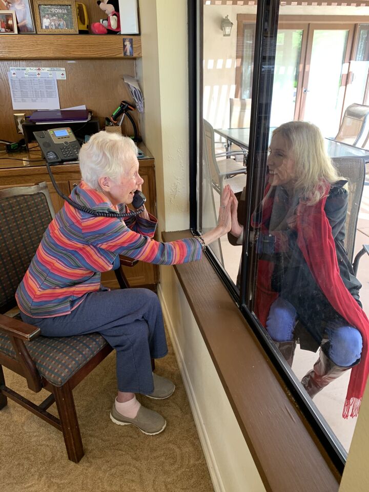 Cadence at Poway Gardens resident Betty Marks speaks to her daughter Cynthia Leigh over the phone and separated by a window on Wednesday, March 18, 2020. Cadence is one of the county's senior living facilities that is prohibiting family visits at this time to prevent residents from coronavirus exposure.