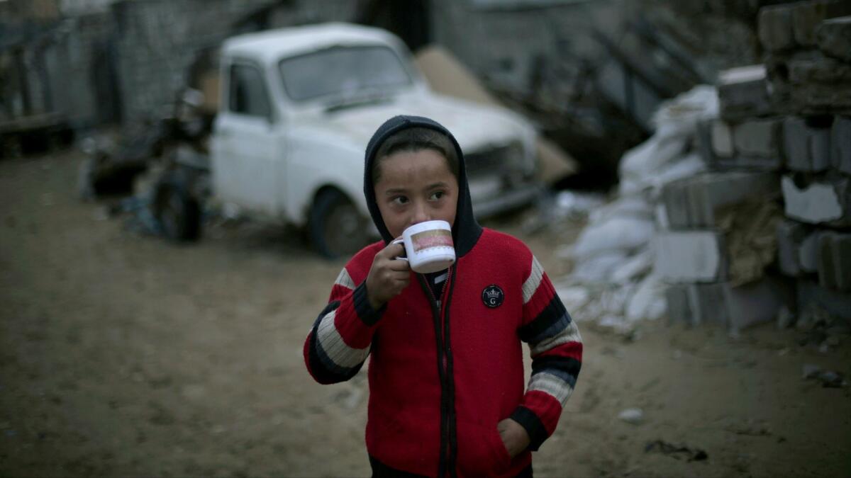 A Palestinian boy drinks hot tea outside his family's residence during rainy, cold weather in a slum on the outskirts of Khan Yunis refugee camp in the southern Gaza Strip.
