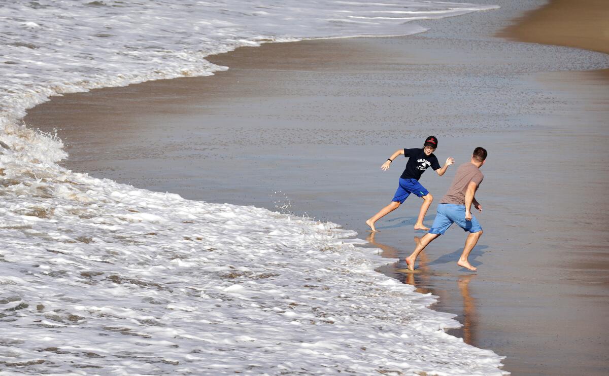 Two boys, wearing long shorts and T-shirts, run barefoot just ahead of a wave. 