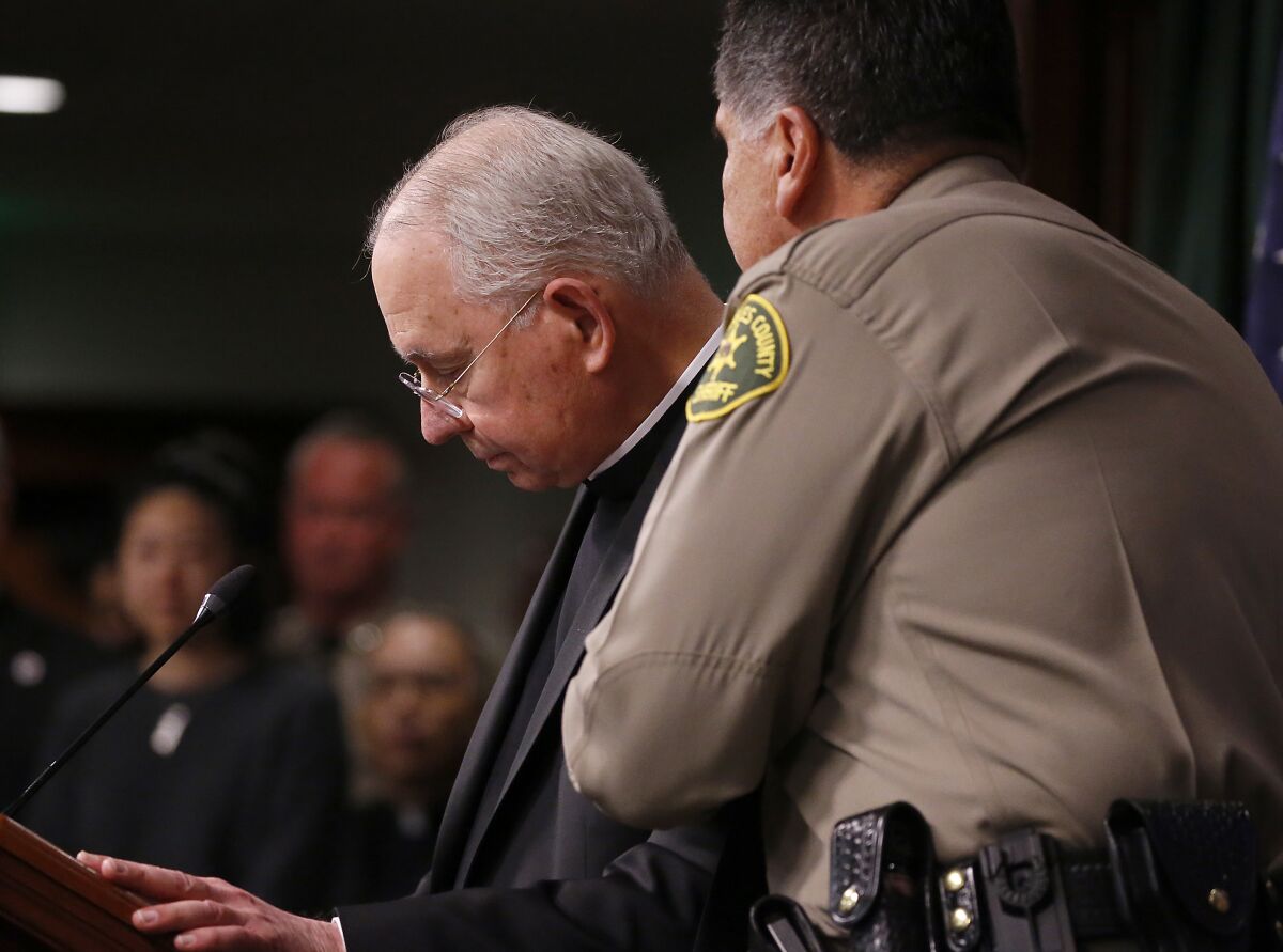 Sheriff Robert Luna, right, comforting L.A. Archbishop José H. Gómez, standing at a lectern